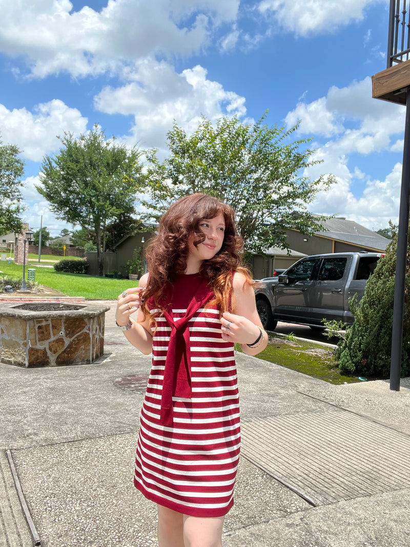 Person wearing a red and white striped dress standing outdoors on a sunny day.