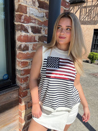 Woman wearing a Queen of Sparkles tank top with an American flag design standing against a brick wall.