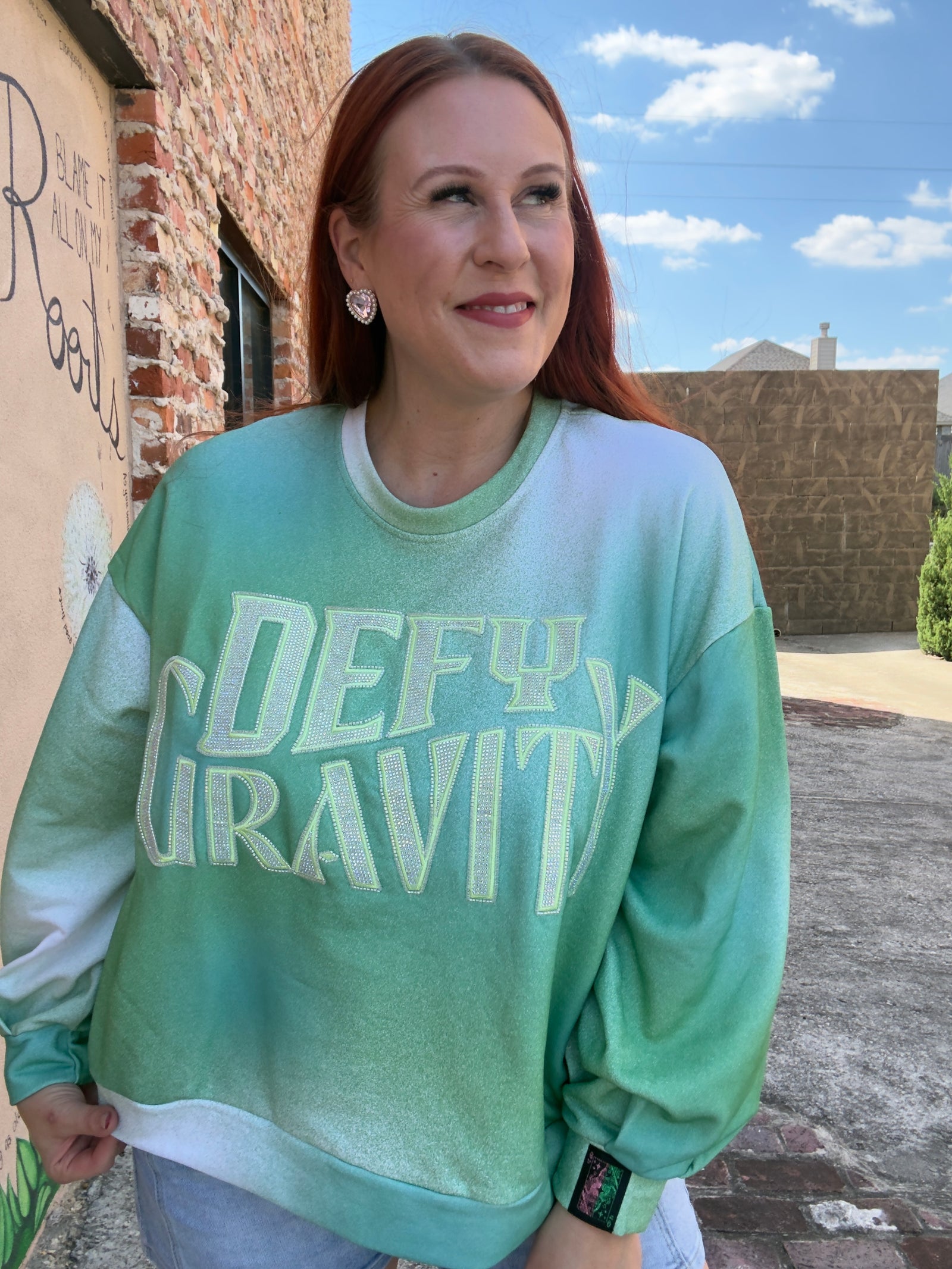 Woman wearing a green sweatshirt with 'DEFY GRAVITY' from the movie Wicked
