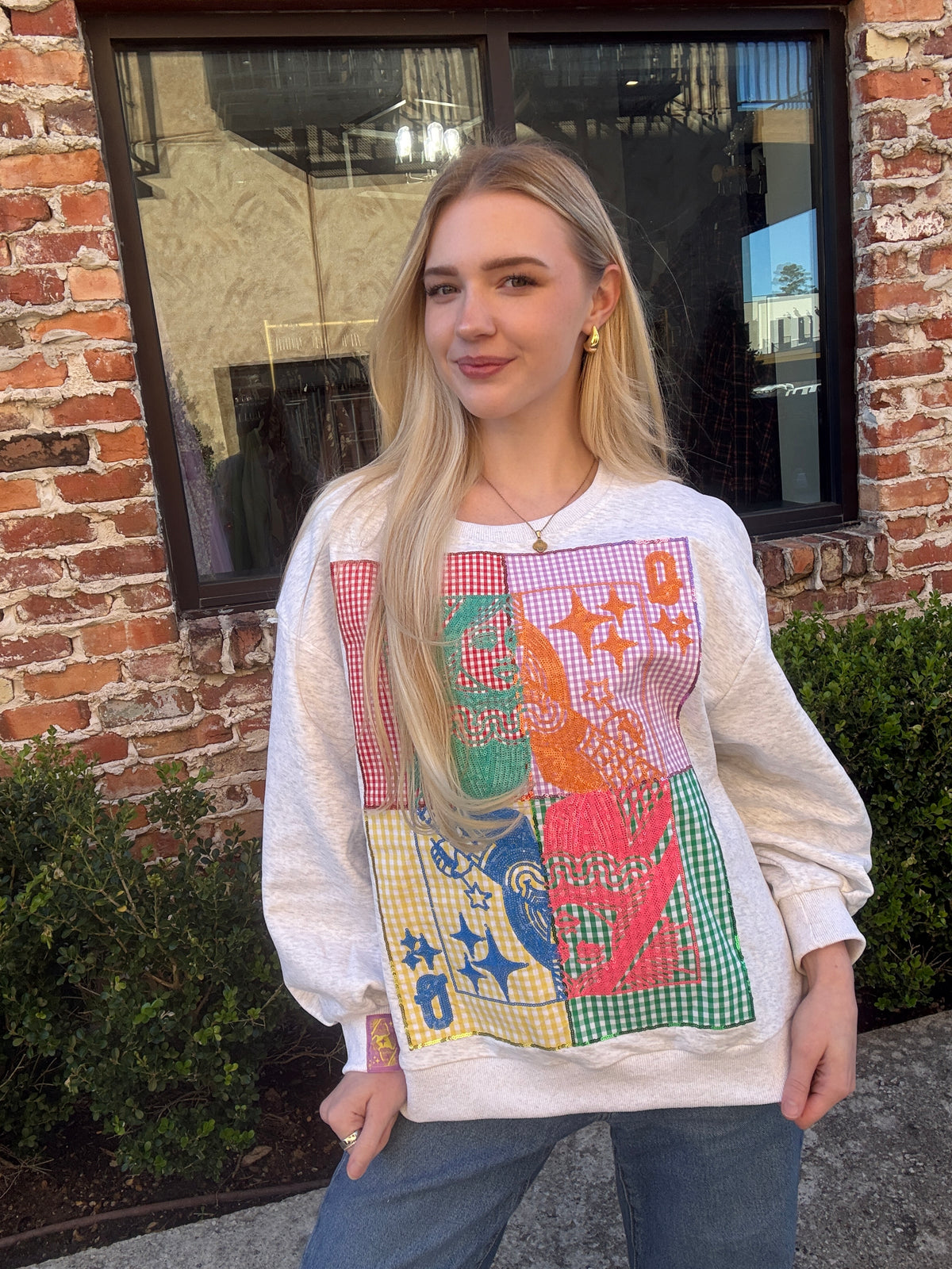 Woman wearing a colorful graphic sweatshirt standing in front of a brick building.