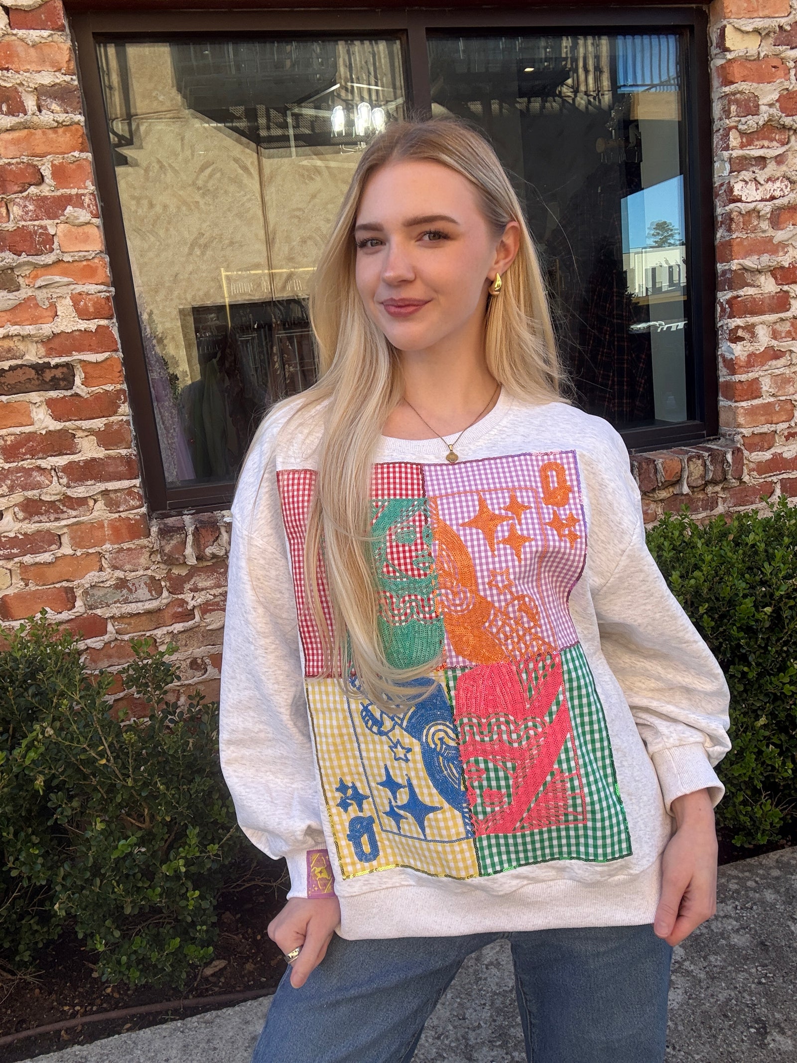 Woman wearing a colorful graphic sweatshirt standing in front of a brick building.